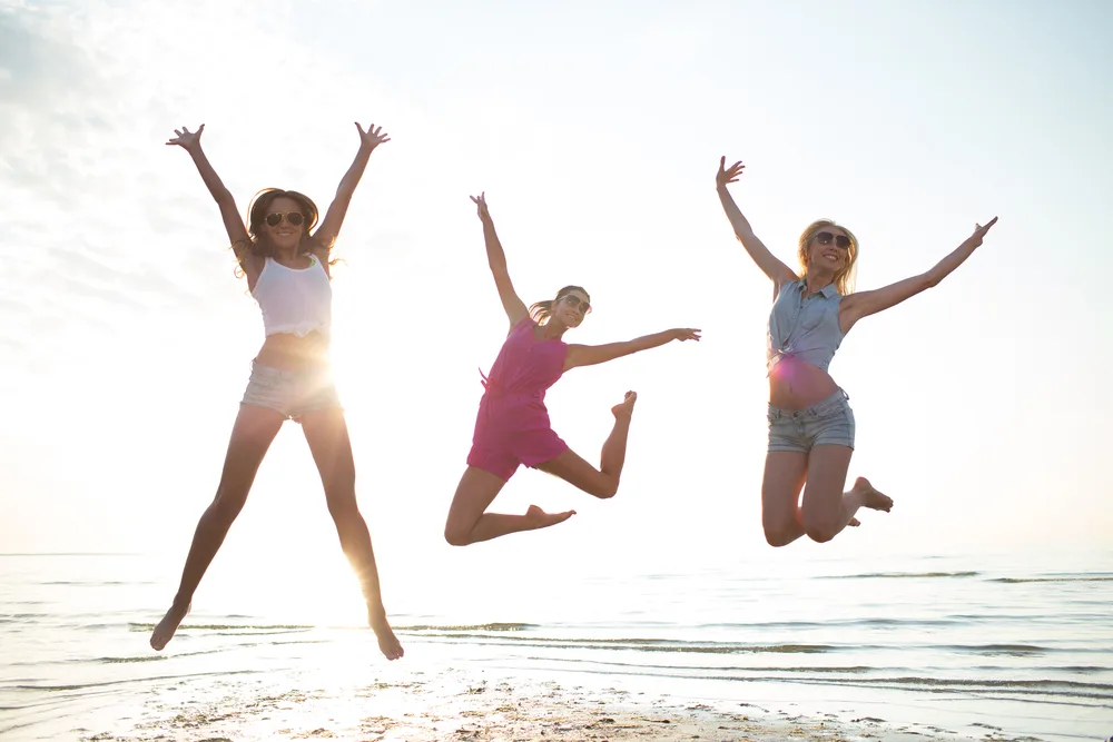 Three woman jump for joy at the beach.