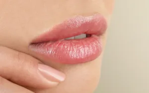 lip filler in lips close up with finger on face with a tan background