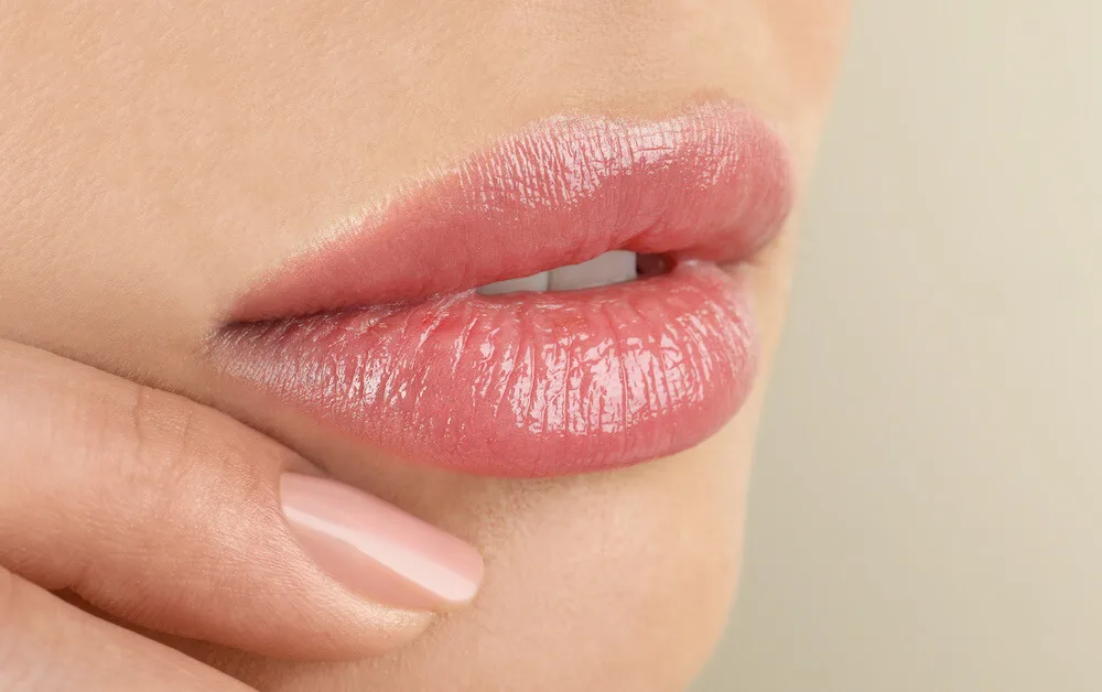 lip filler in lips close up with finger on face with a tan background