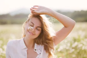A peaceful woman holding a flower over her face while smiling.