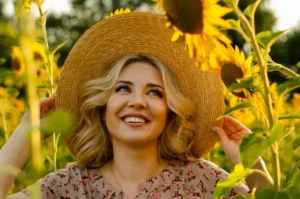 A woman holding her hat to block her from sun while in a sunflower field.