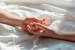 Partial view of couple in live holding hands while lying in bed together.