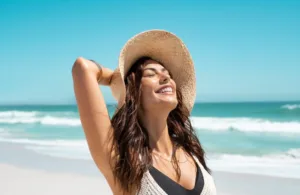 A woman smiling up at the sun at the beach in California.
