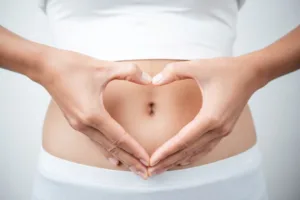 A woman forming a heart with her hands above her abdomen in relation to women's health.