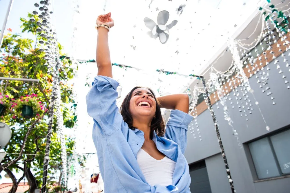 Young woman on street laughing with hands in air.