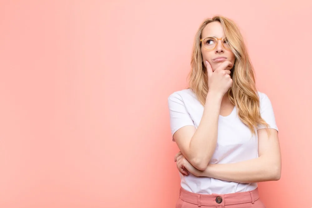 A woman thinking, feeling doubtful and confused, with different options, wondering which decision to make against flat color wall.